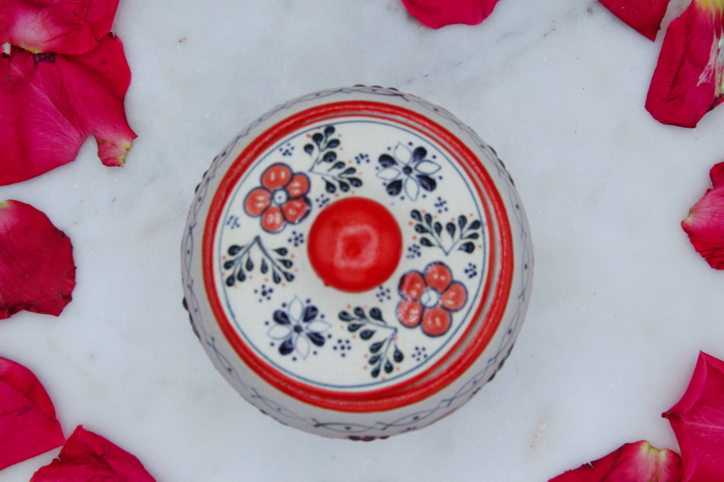 Top view of the handmade artisanal candle in a red floral design talavera with a closed lid on its side. Custom made by Artisan in Mexico. 100% All Natural Soy Candle. Reuse the talavera as home decor or storage.