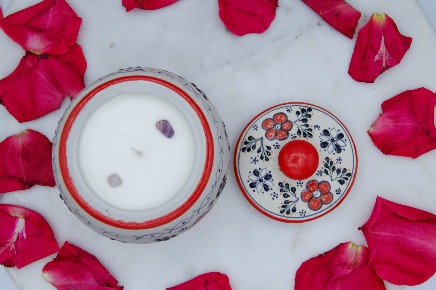 Top view of the handmade artisanal candle in a red floral design talavera with an open lid on its side. Custom made by Artisan in Mexico. 100% All Natural Soy Candle. Reuse the talavera as home decor or storage.