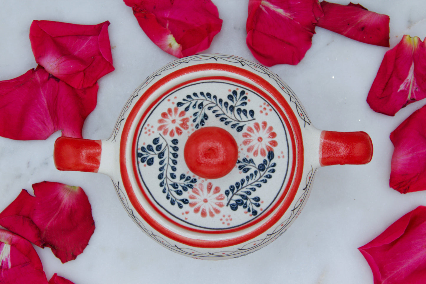 Top view of the handmade artisanal candle in a red floral design talavera with handles on both sides and a closed lid. Custom made by Artisan in Mexico. 100% All Natural Soy Candle. Reuse the talavera as home decor or storage.