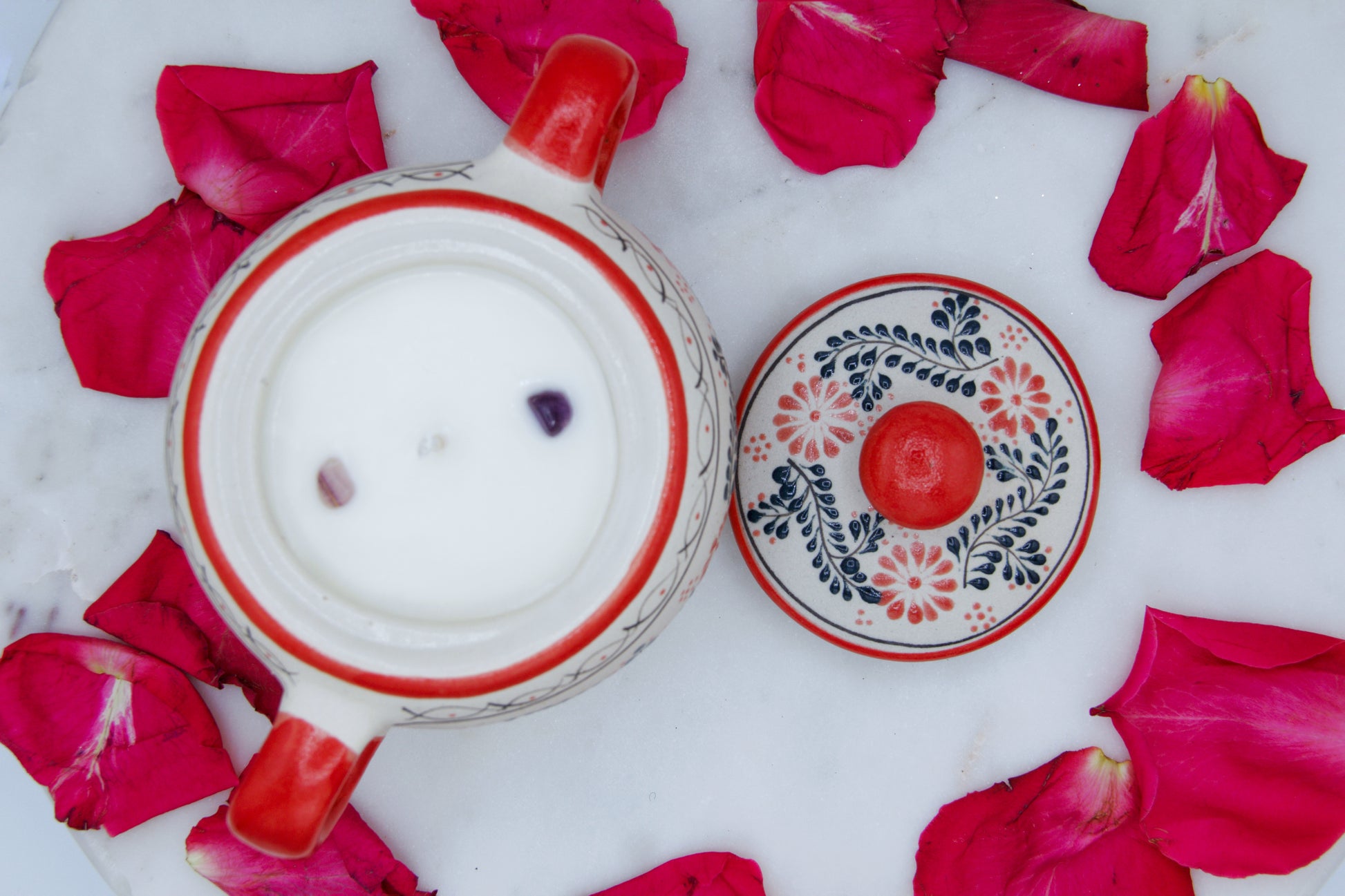 Top view of the handmade artisanal candle in a red floral design talavera with handles on both sides and an open lid placed on the side. Custom made by Artisan in Mexico. 100% All Natural Soy Candle. Reuse the talavera as home decor or storage.