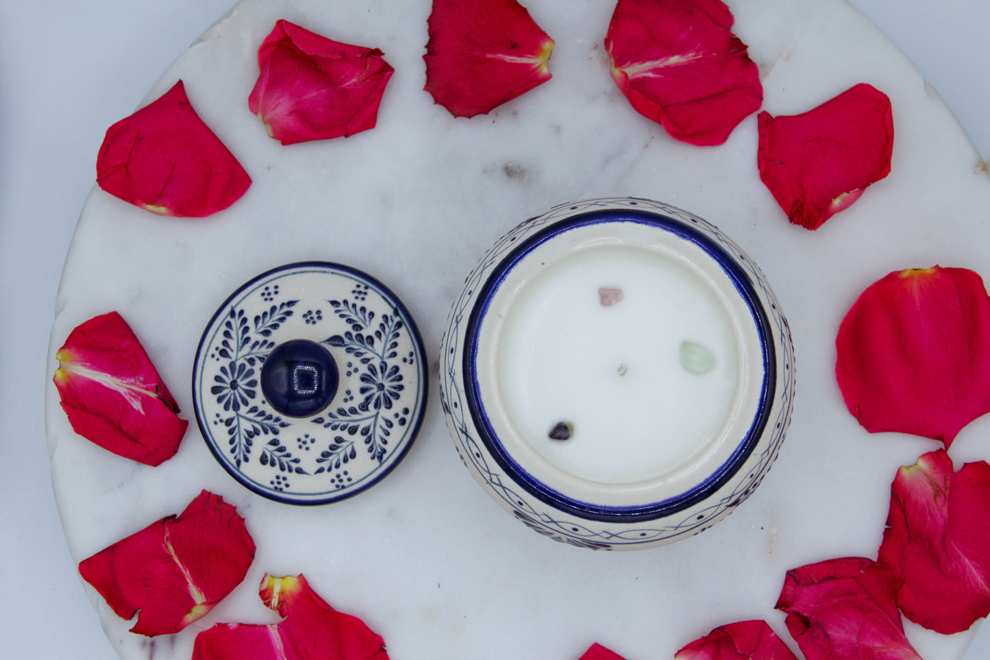 Top view of the handmade artisanal candle in a red floral design talavera with an open lid on its side. Custom made by Artisan in Mexico. 100% All Natural Soy Candle. Reuse the talavera as home decor or storage.