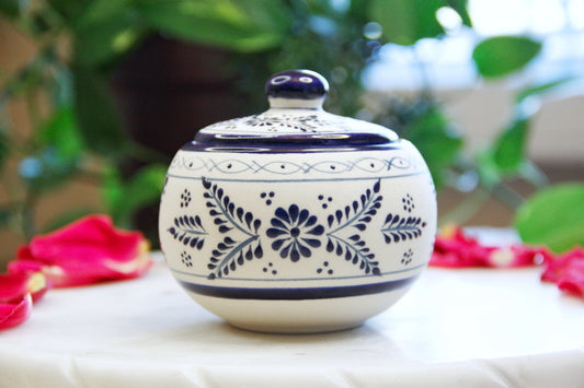 Front view of the handmade artisanal candle in a blue floral design talavera with a closed lid on its side. Custom made by Artisan in Mexico. 100% All Natural Soy Candle. Reuse the talavera as home decor or storage.