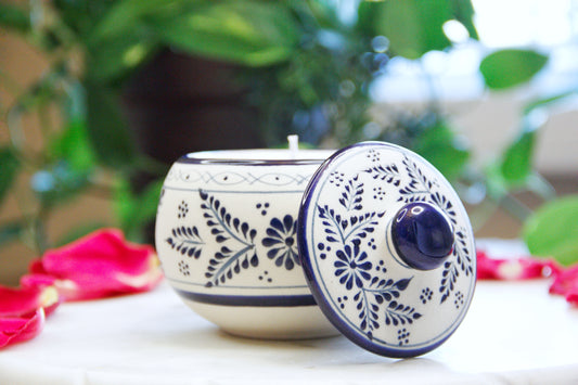 Front view of the handmade artisanal candle in a blue floral design talavera with an open lid on its side. Custom made by Artisan in Mexico. 100% All Natural Soy Candle. Reuse the talavera as home decor or storage.