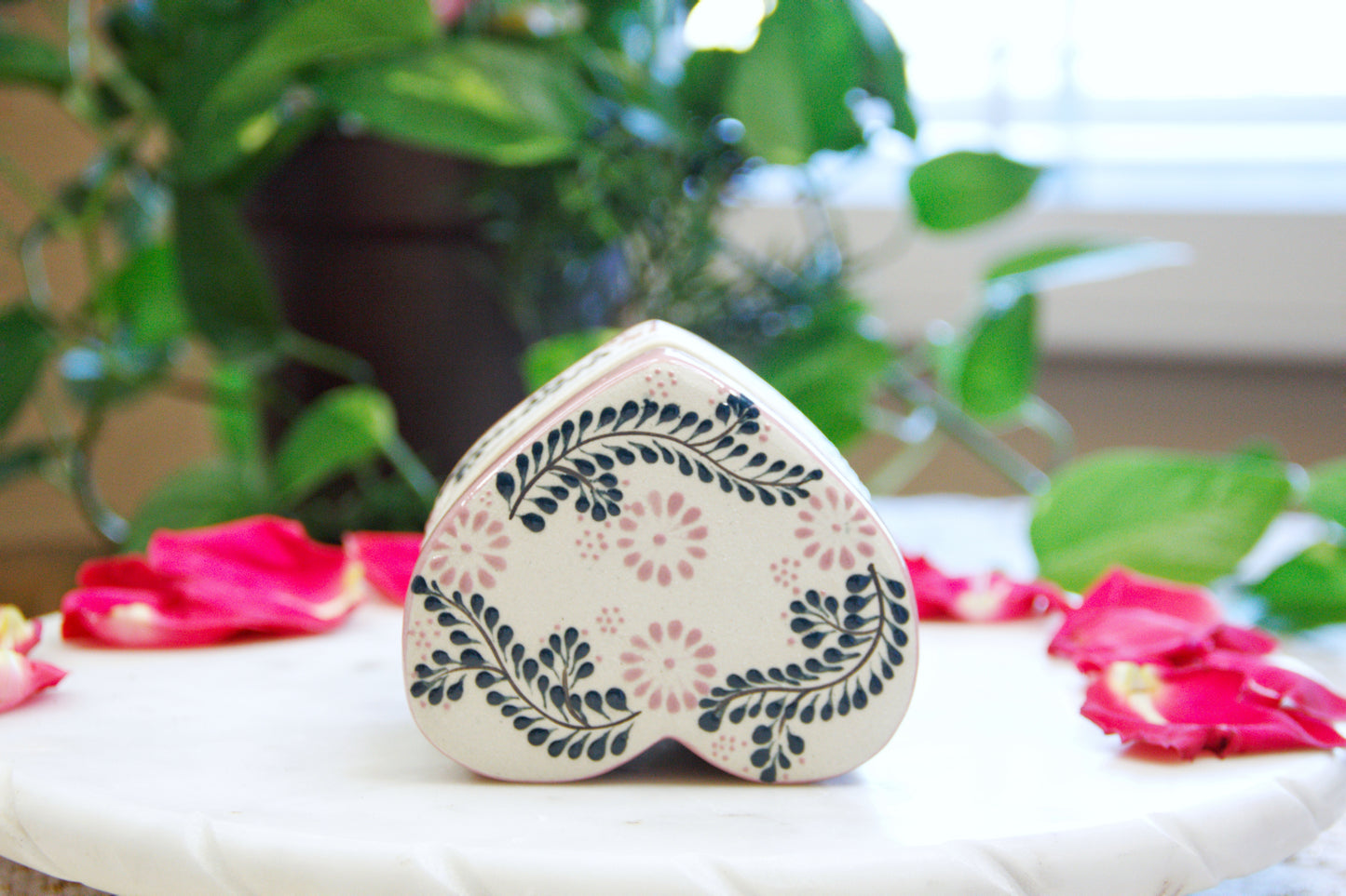 upside down view of an Artisanal candle in a beautiful heart shaped talavera. Handmade pink floral design with a closed lid. Handcrafted by Artisan in Mexico City. 100% All Natural Soy Candle. Reuse the talavera as home decor or storage.