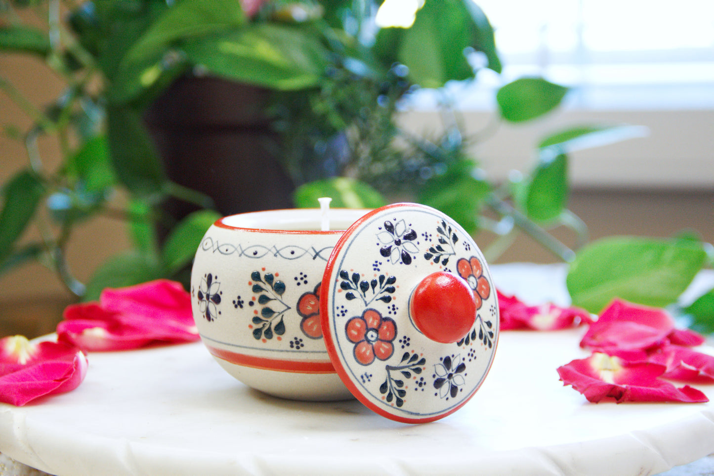 Front view of the handmade artisanal candle in a red floral design talavera with an open lid on its side. Custom made by Artisan in Mexico. 100% All Natural Soy Candle. Reuse the talavera as home decor or storage.