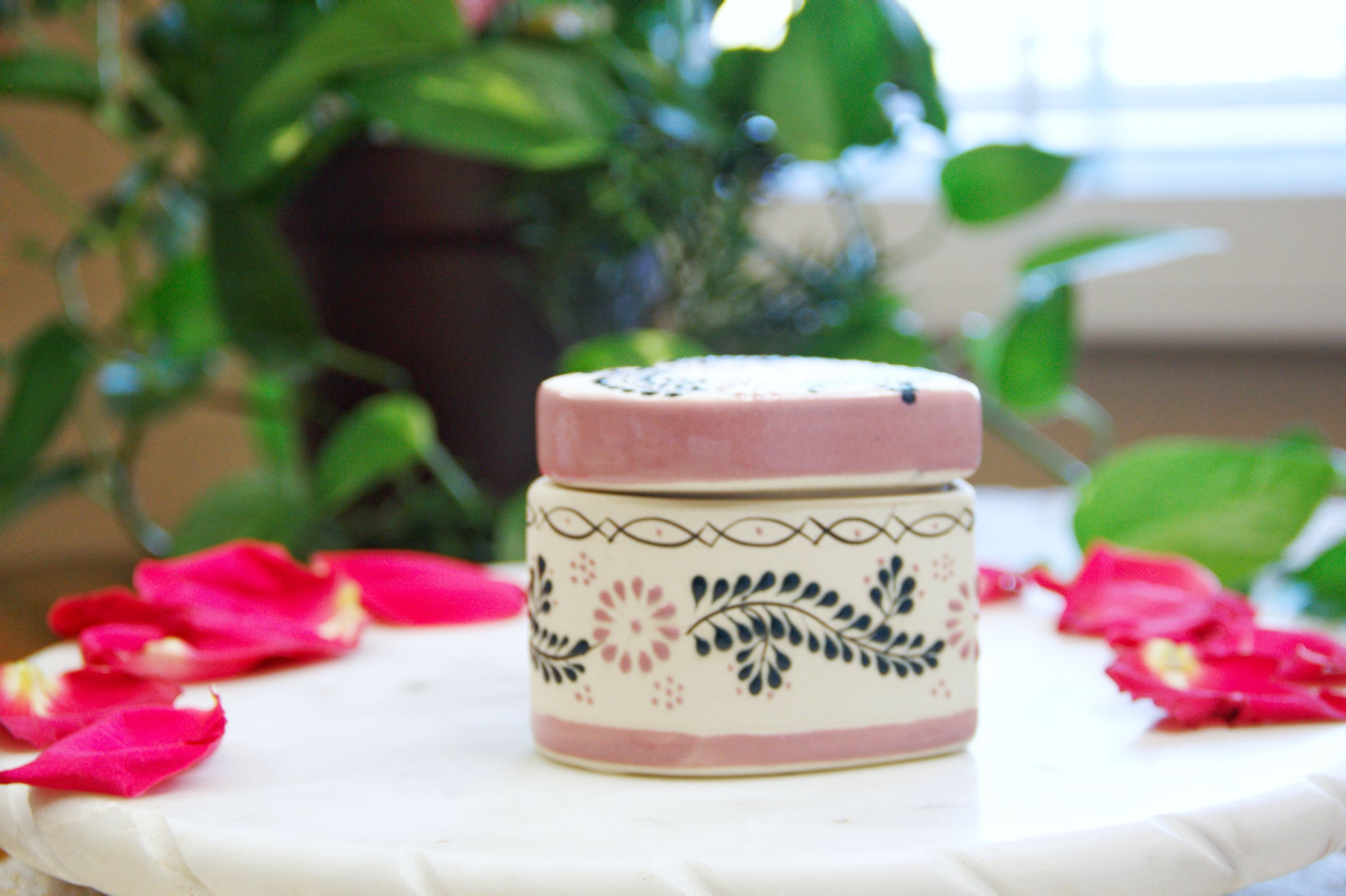 side view of an Artisanal candle in a beautiful heart shaped talavera. Handmade pink floral design with a closed lid. Handcrafted by Artisan in Mexico City. 100% All Natural Soy Candle. Reuse the talavera as home decor or storage.