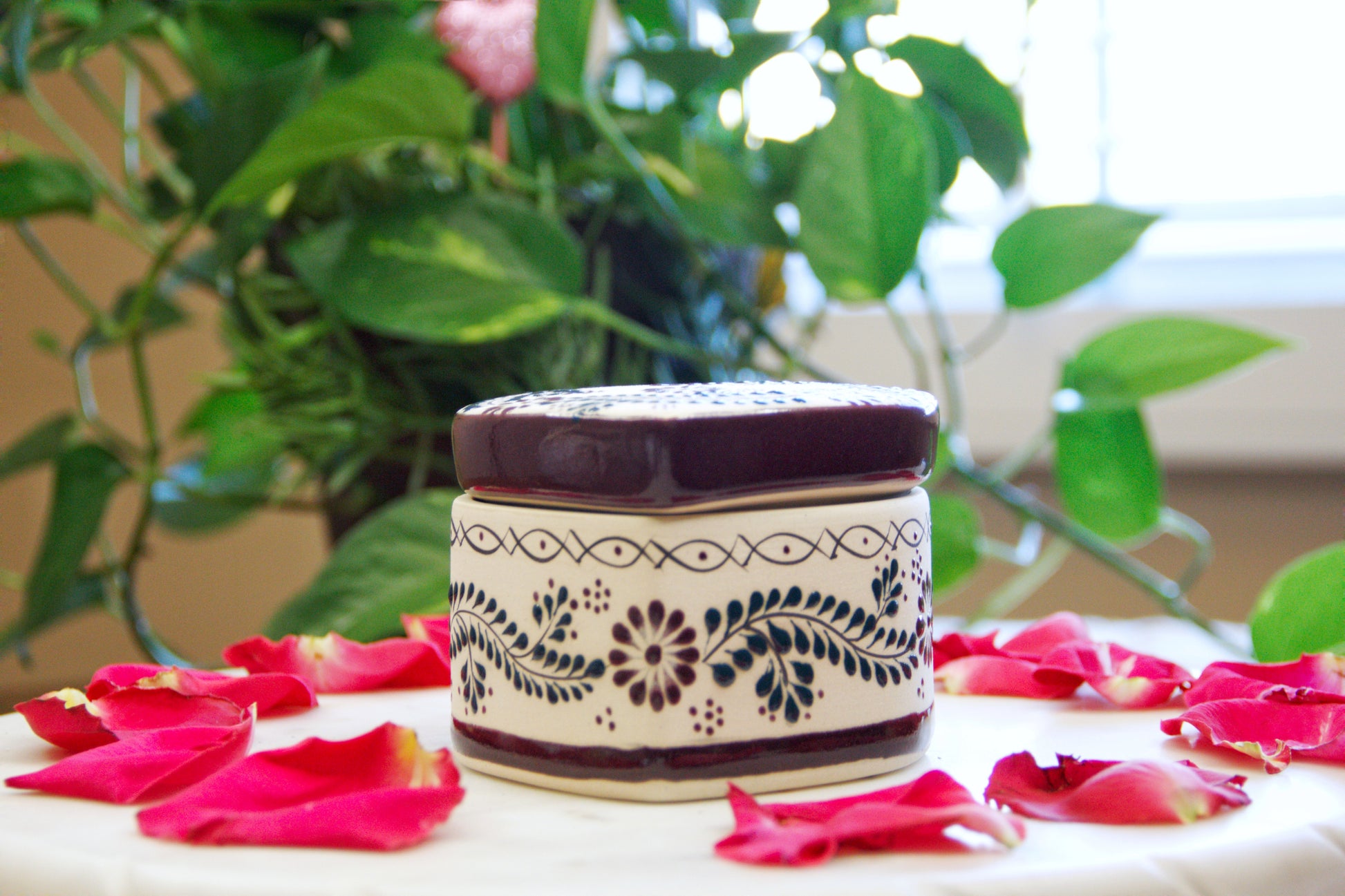side view of an Artisanal candle in a beautiful heart shaped talavera. Handmade brown floral design with a closed lid. Handcrafted by Artisan in Mexico City. 100% All Natural Soy Candle. Reuse the talavera as home decor or storage.