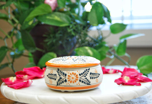 handmade artisanal candle in an orange floral design talavera with a closed lid. Custom made by Artisan in Mexico. 100% All Natural Soy Candle. Reuse the talavera as home decor or storage