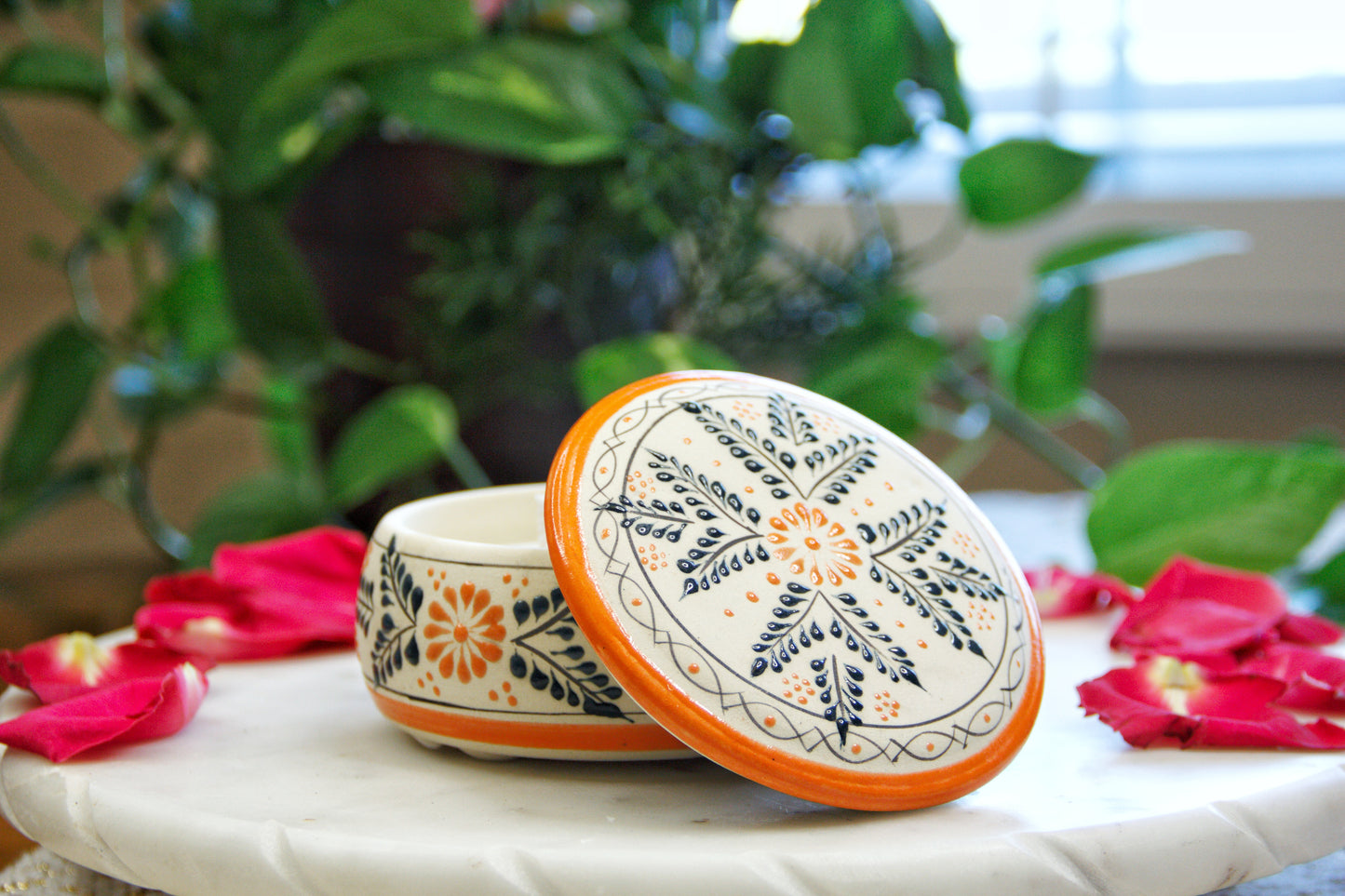 handmade artisanal candle in an orange floral design talavera with an open lid. Custom made by Artisan in Mexico. 100% All Natural Soy Candle. Reuse the talavera as home decor or storage