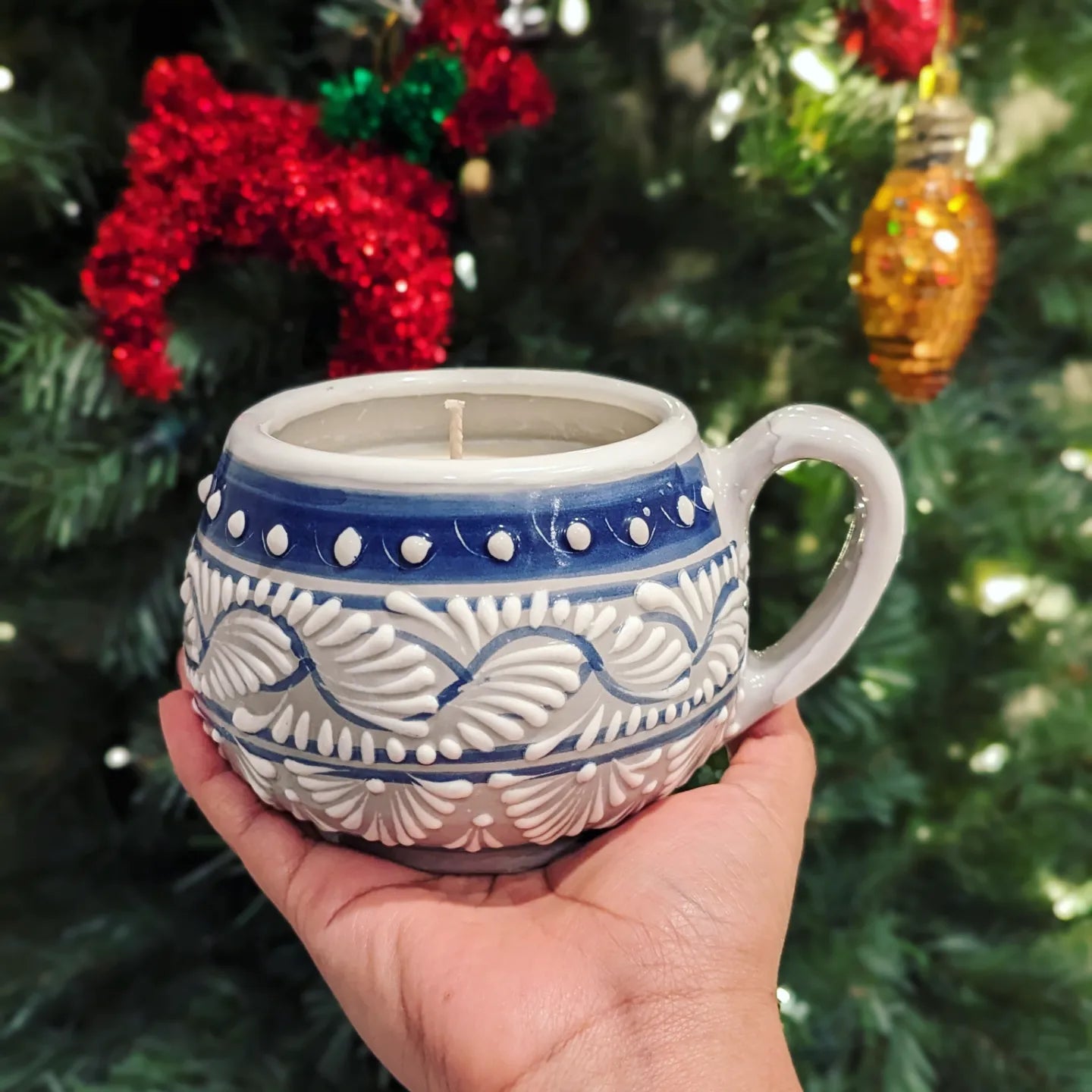 Artisanal candle placed on a hand. Blue Grey color with white hand painted design. Handcrafted by Artisan in Puebla, Mexico. 100% All Natural Soy Candle. Reuse the talavera as home decor or storage.