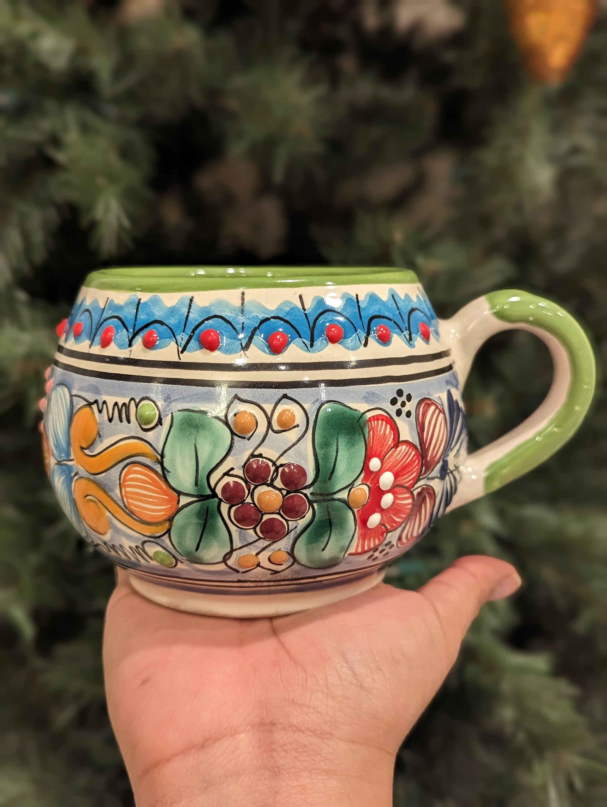 A hand holding an Artisanal candle in a beautiful multicolored talavera cup with a handle. Handcrafted by Artisan in Puebla, Mexico. 100% All Natural Soy Candle. Reuse the talavera as home decor or storage.