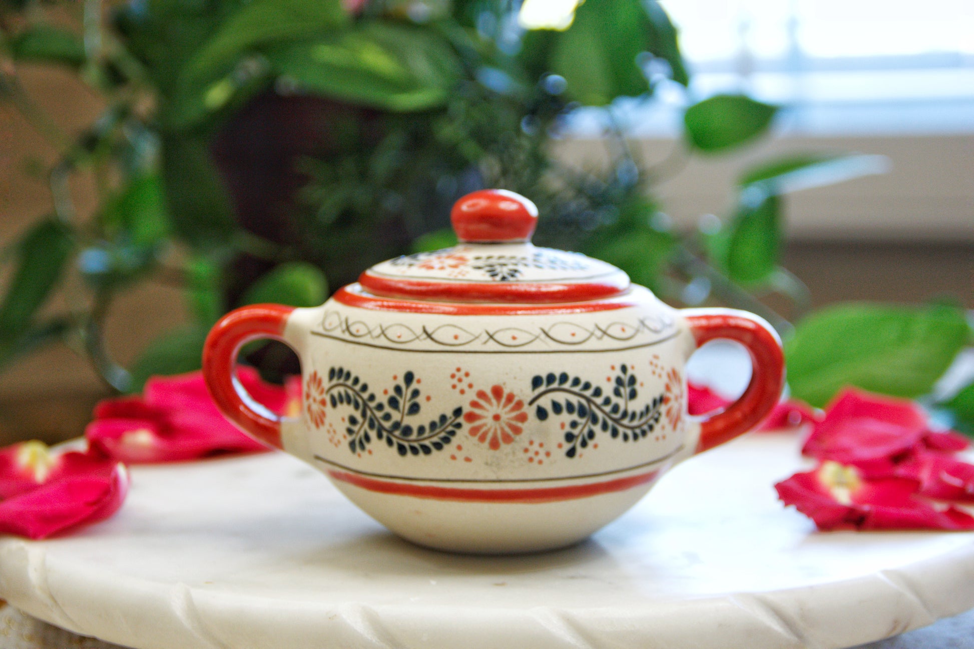 Front view of the handmade artisanal candle in a red floral design talavera with handles on both sides and a closed lid. Custom made by Artisan in Mexico. 100% All Natural Soy Candle.  Reuse the talavera as home decor or storage.